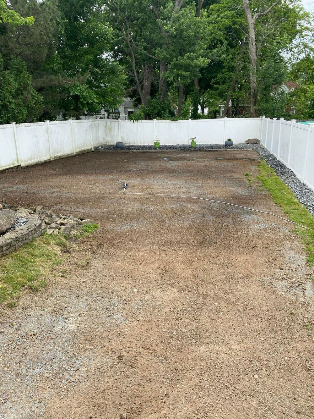 Bare backyard undergoing landscaping with gravel and fenced area for future garden plans.