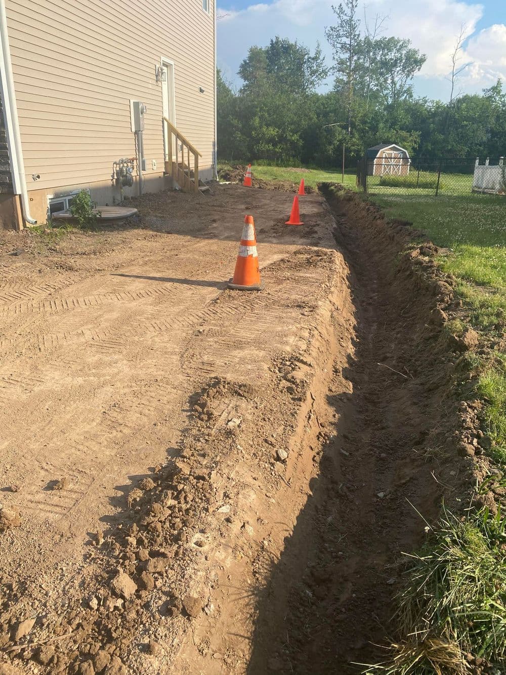 Excavated trench alongside house with traffic cones marking safe areas.