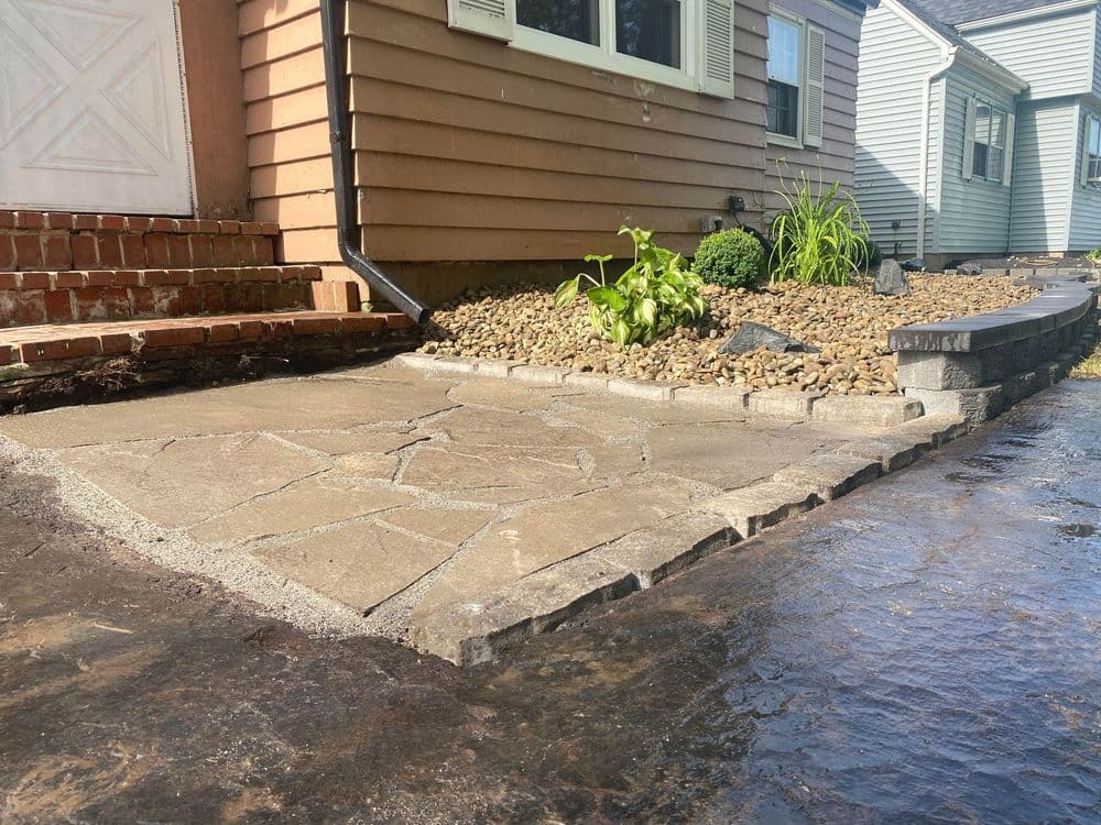 Stone walkway and landscaped entrance leading to a house with a textured driveway and plants.