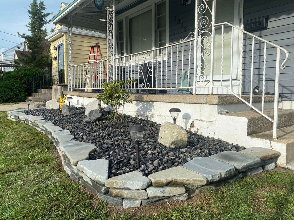 Front yard landscaping with stone borders, decorative rocks, and garden lights near a porch.