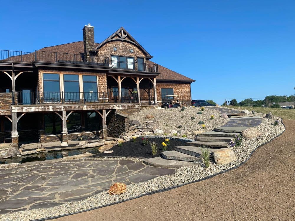 Luxury stone house with expansive patio, landscaped yard, and clear blue sky.