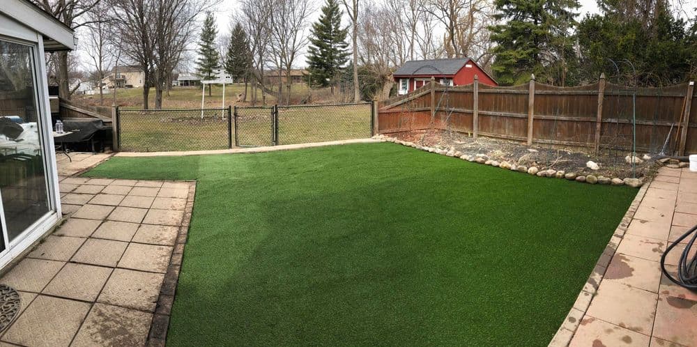 Lush artificial turf backyard with fenced area and landscaped stones, ideal for outdoor activities.