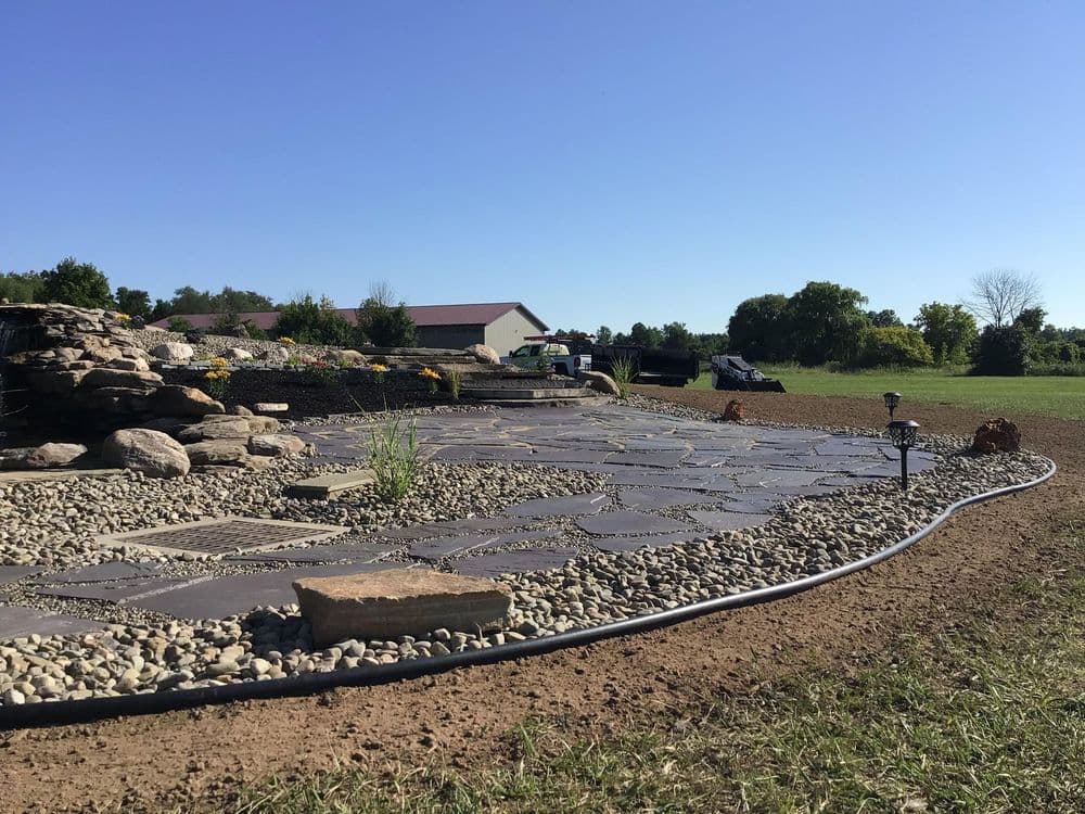 Stone garden path with decorative rocks and plants under a clear blue sky.
