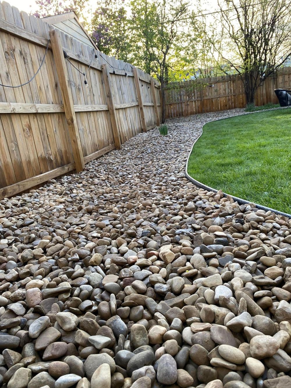 Gravel pathway bordered by wooden fence and greenery in backyard garden setting.