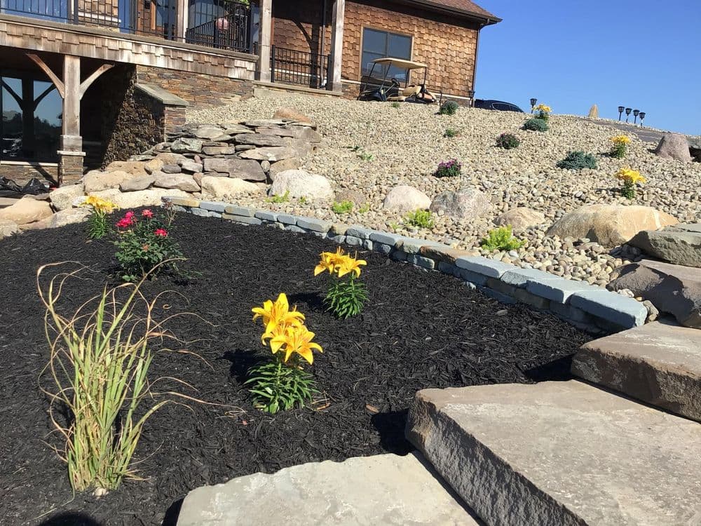 Landscape design featuring yellow lilies and colorful flowers in a modern garden with stone accents.