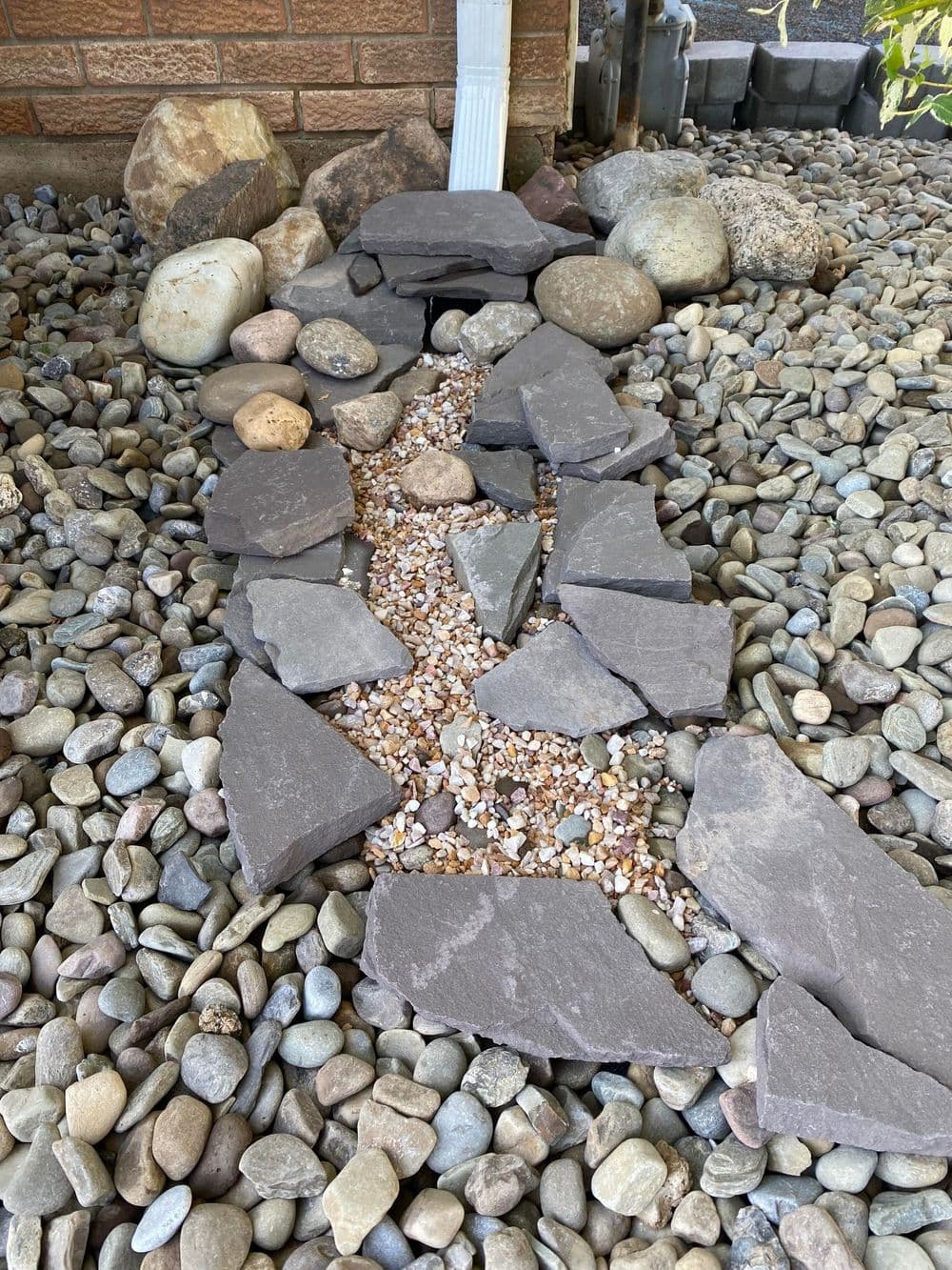 Garden walkway made of gray stones and pebbles, surrounded by larger decorative rocks.