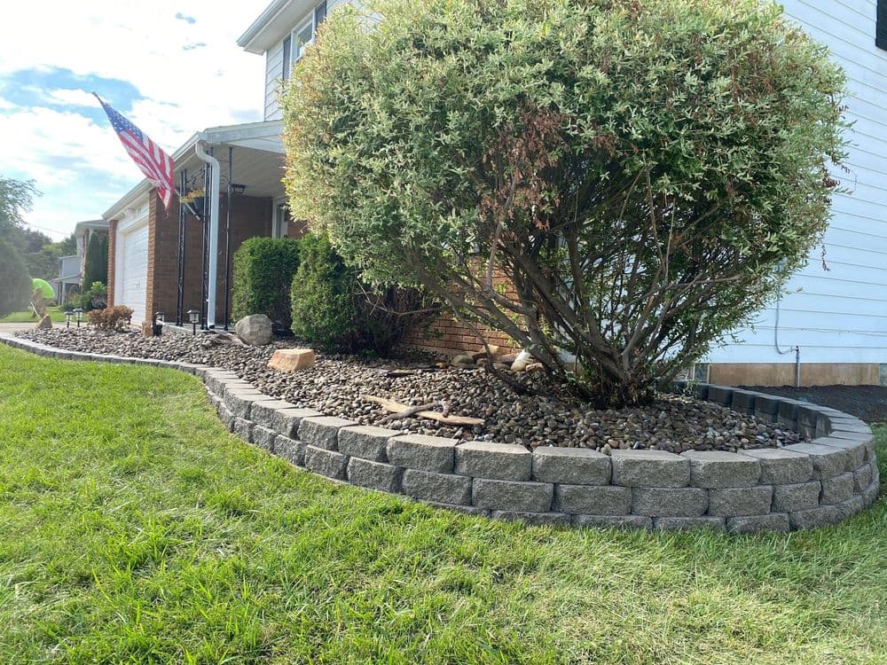 Landscaped garden with stone border, shrubs, and American flag in residential area.