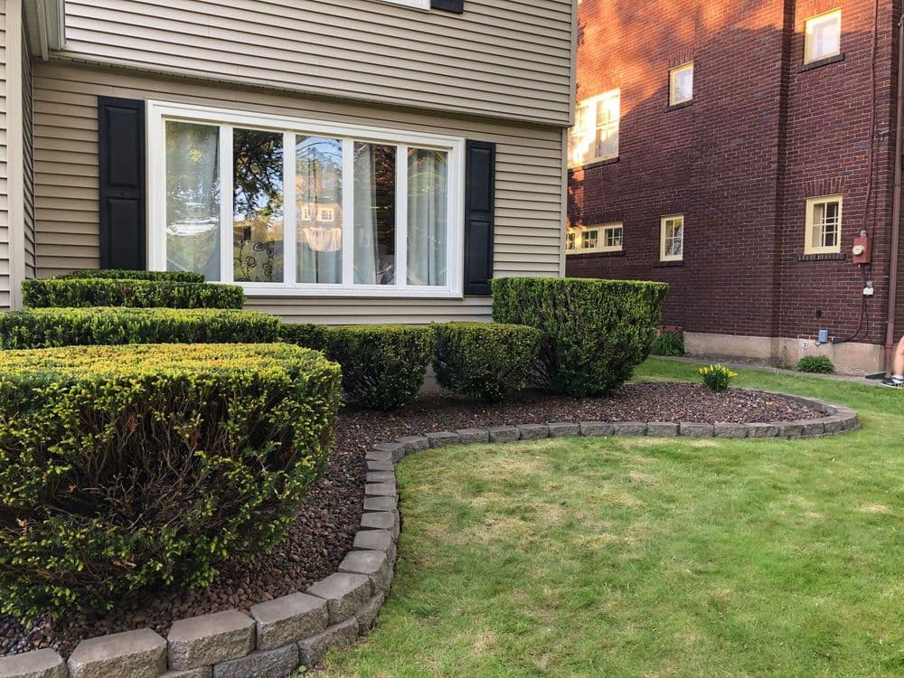 Landscape view of a well-manicured garden with hedges and stone edging beside a home.