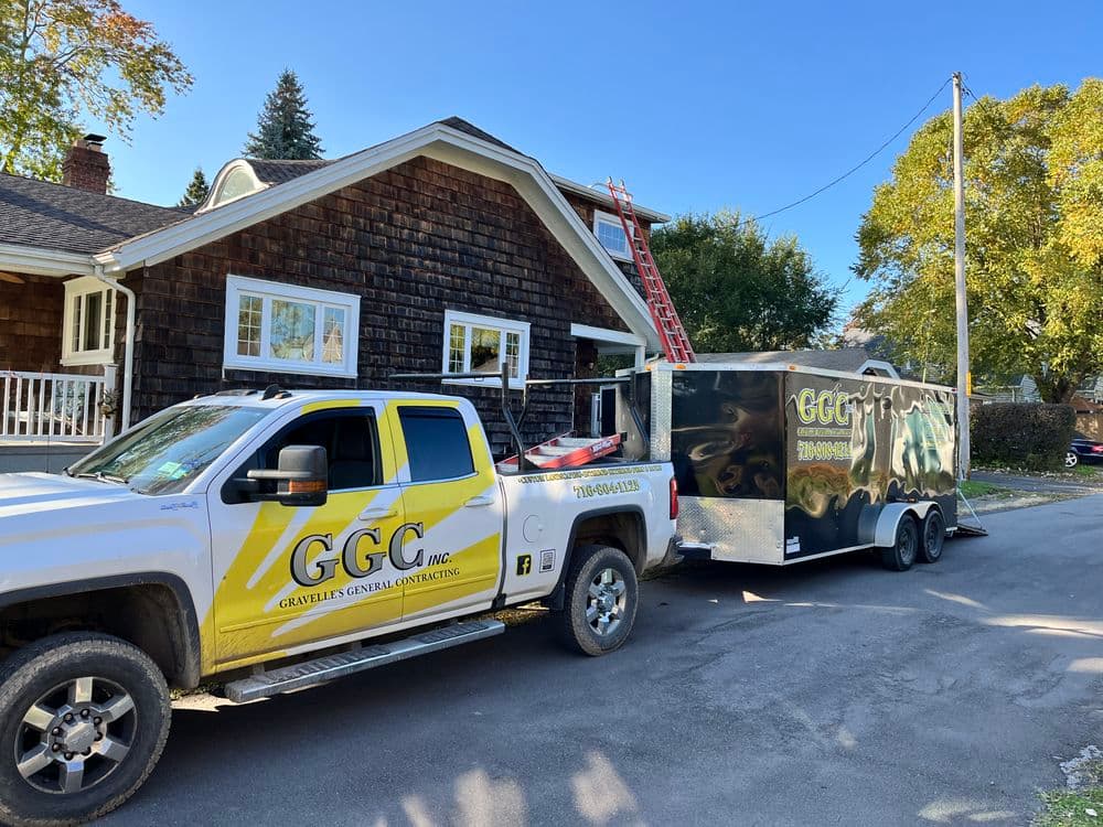 Yellow and black construction truck with trailer parked outside a home for renovation services.