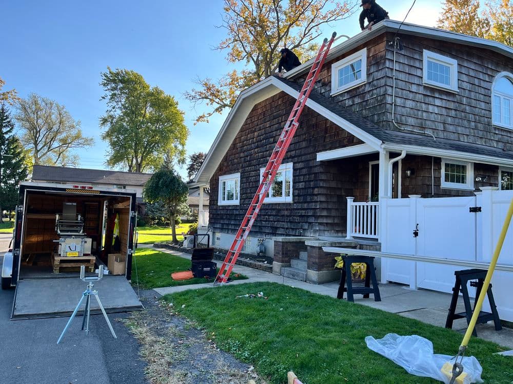 Roofers using a ladder on a home for repairs, with a truck and tools nearby.