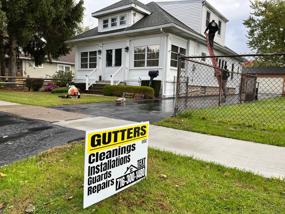 Gutters service sign in front of a house with a worker cleaning gutters above.