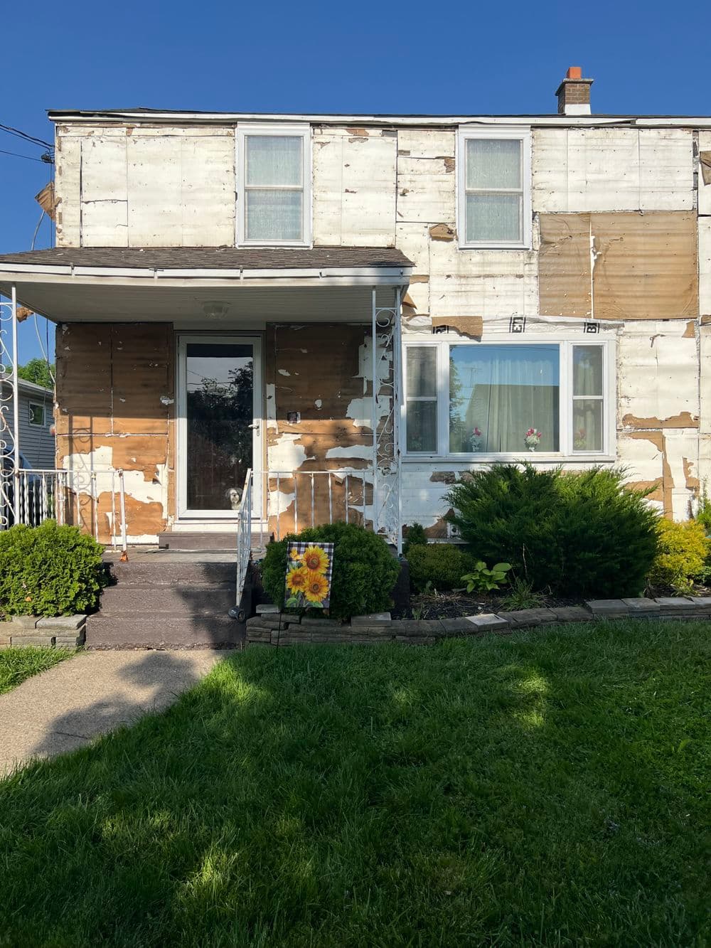 Front view of a weathered two-story home with landscaping and a sunflower decoration.