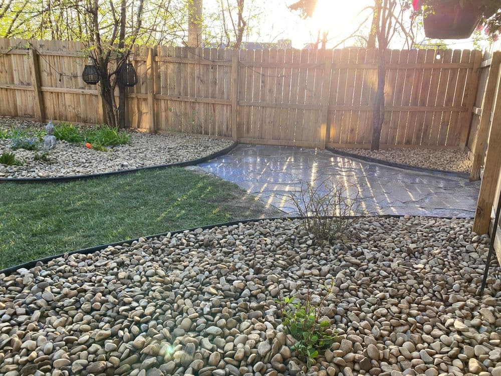Well-landscaped backyard with gravel, stone path, and wooden fence lit by sunlight.
