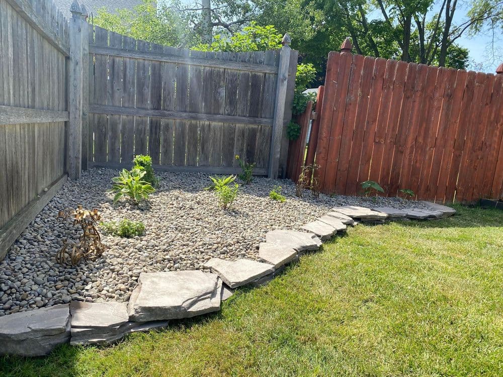 Rock garden with gravel, plants, and stone pathway bordered by wooden fences.