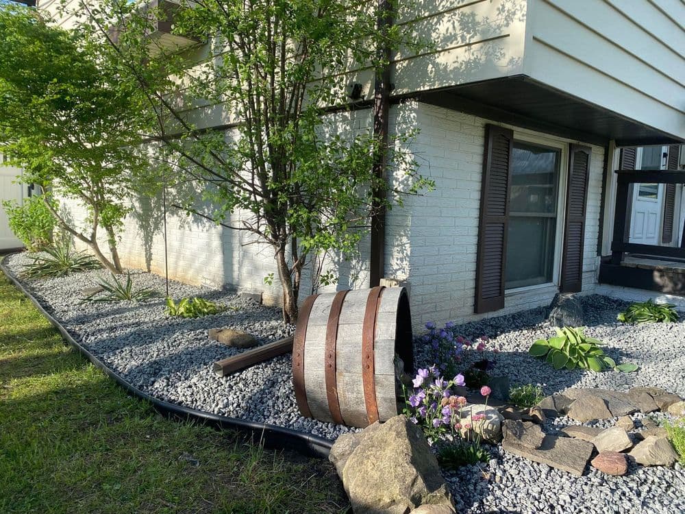 Landscaped home exterior featuring a wooden barrel, flowers, and gravel.