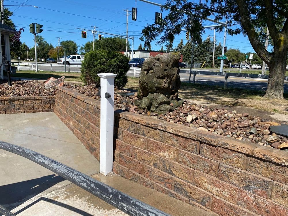 Stone wall feature with rocks and a decorative boulder near a traffic intersection.