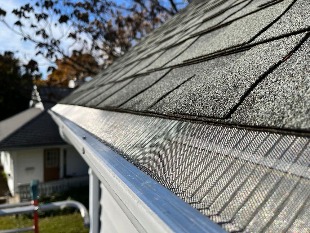 Close-up of a roof with gray shingles and metal flashing under clear blue sky.