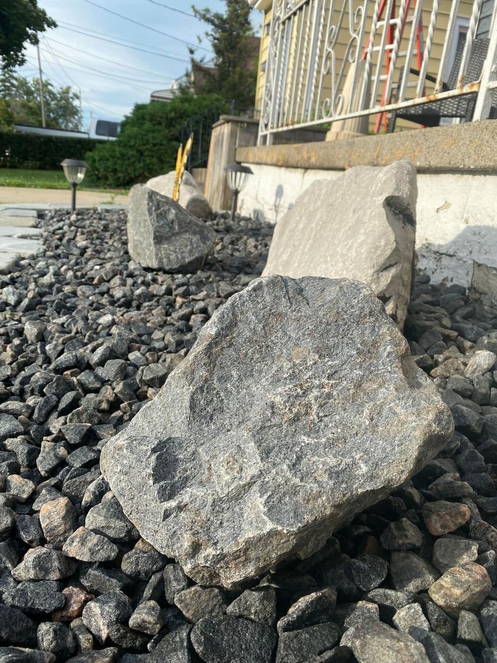 Large gray rocks on gravel landscape near a residential entrance. Decorative outdoor design.