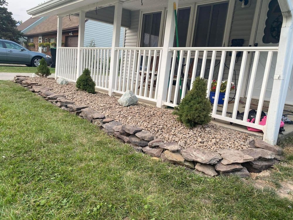 Landscaped garden with stone border, gravel ground cover, and evergreen shrubs near porch.