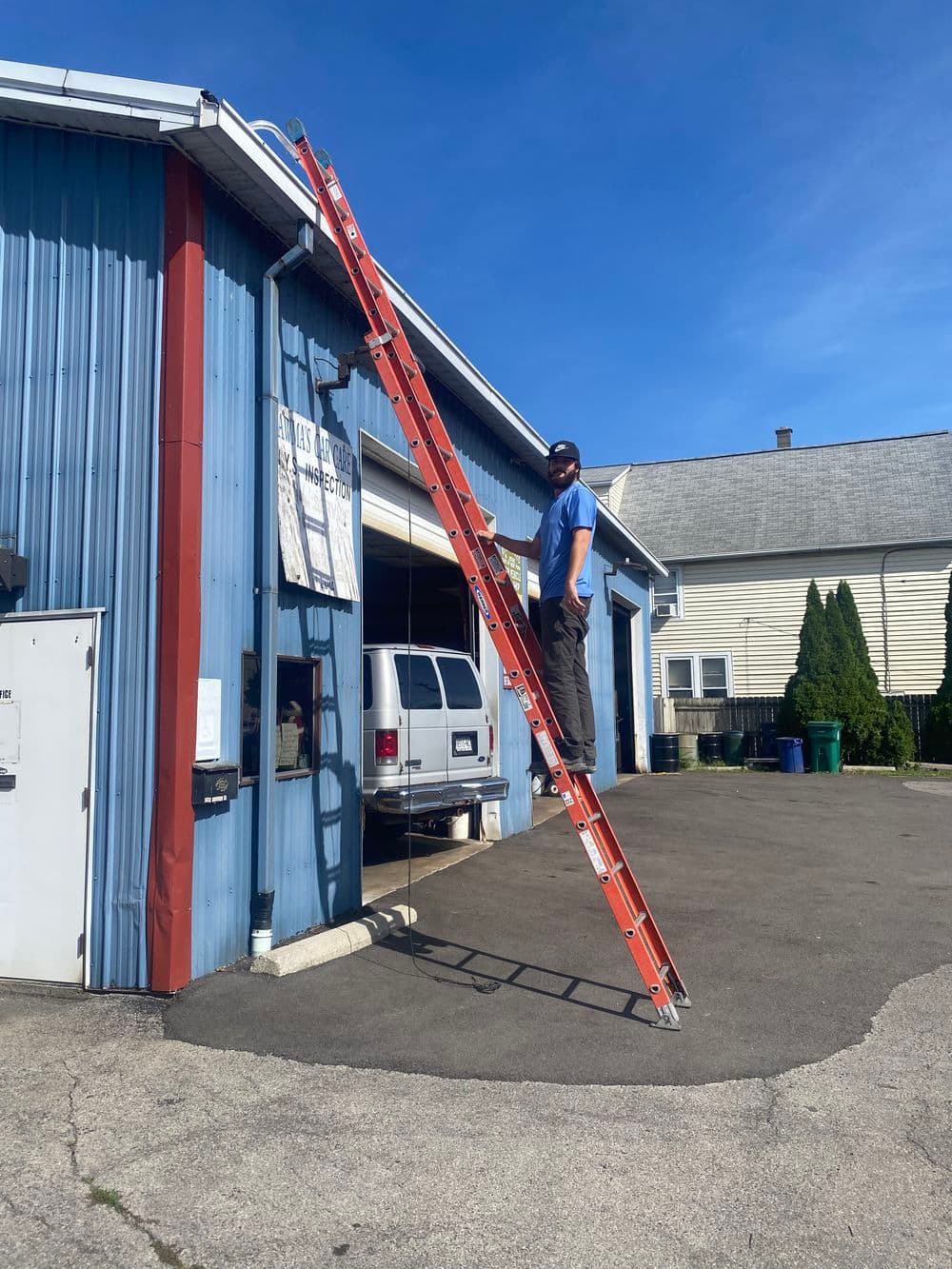Worker on a tall orange ladder performing maintenance on a blue commercial building.
