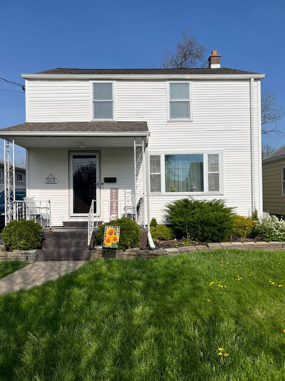 Two-story white house with a manicured lawn and colorful flower signage in the front yard.