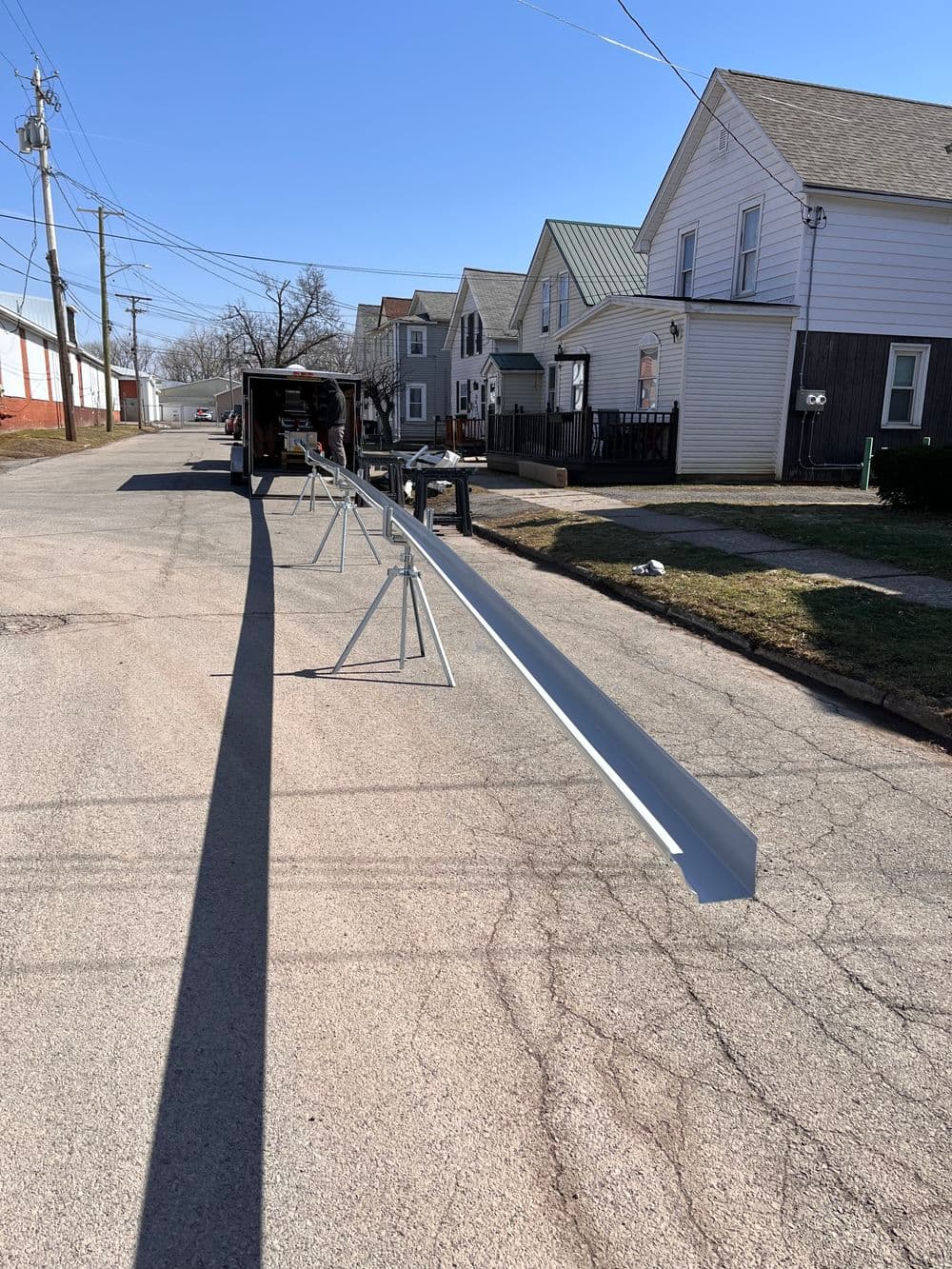 Metal framing on sawhorses in residential area with houses and utility poles in background.
