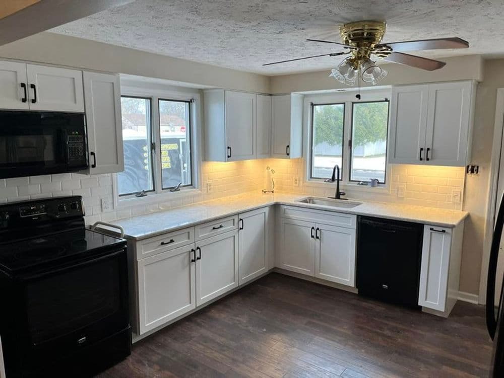 Modern kitchen with white cabinets, marble countertops, and black appliances, featuring a ceiling fan.