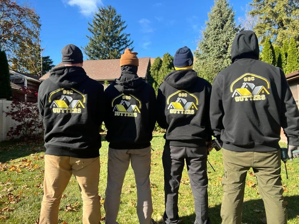 Four individuals in black hoodies with "GSC Gutters" logo, standing outdoors in a yard.