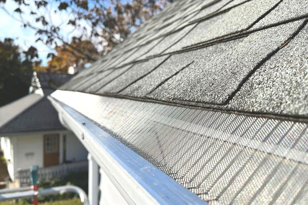 Close-up of a roof edge with shingles and a gutter guard installed on a residential home.