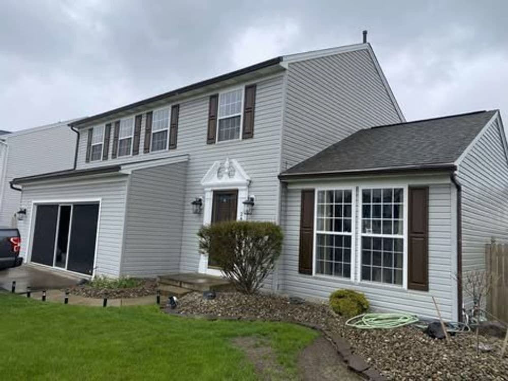 Two-story gray house with front porch and lush green lawn under cloudy sky.