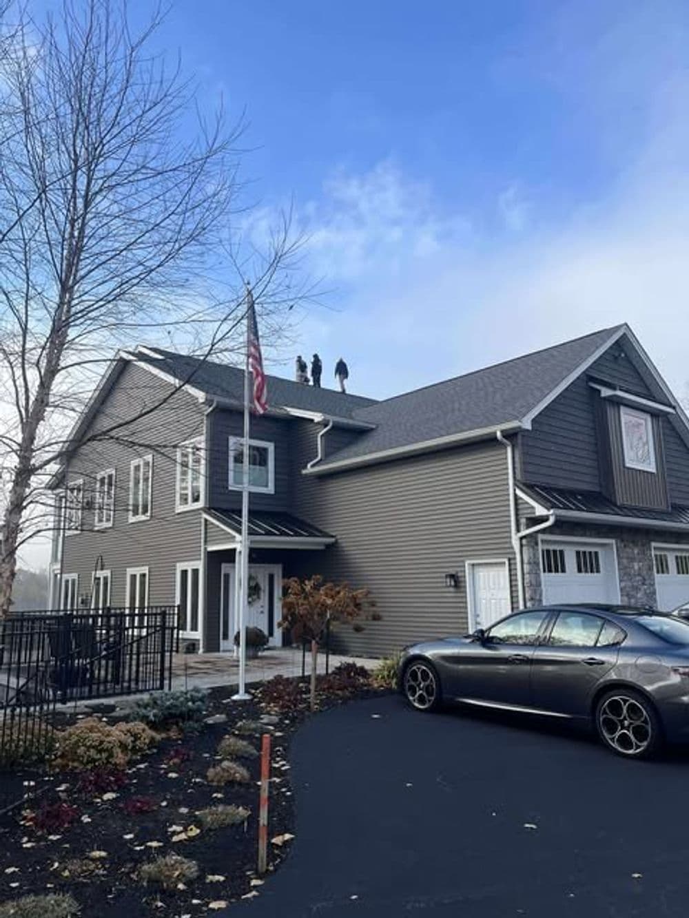 Workers on a roof of a two-story building with an American flag and a parked car.