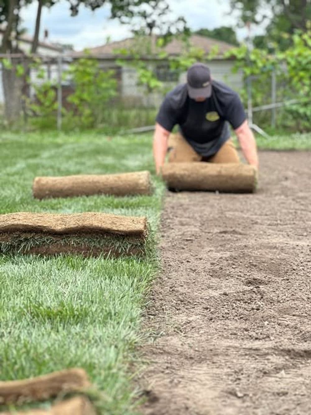 Person laying sod on a freshly prepared lawn, with rolled turf visible in the foreground.
