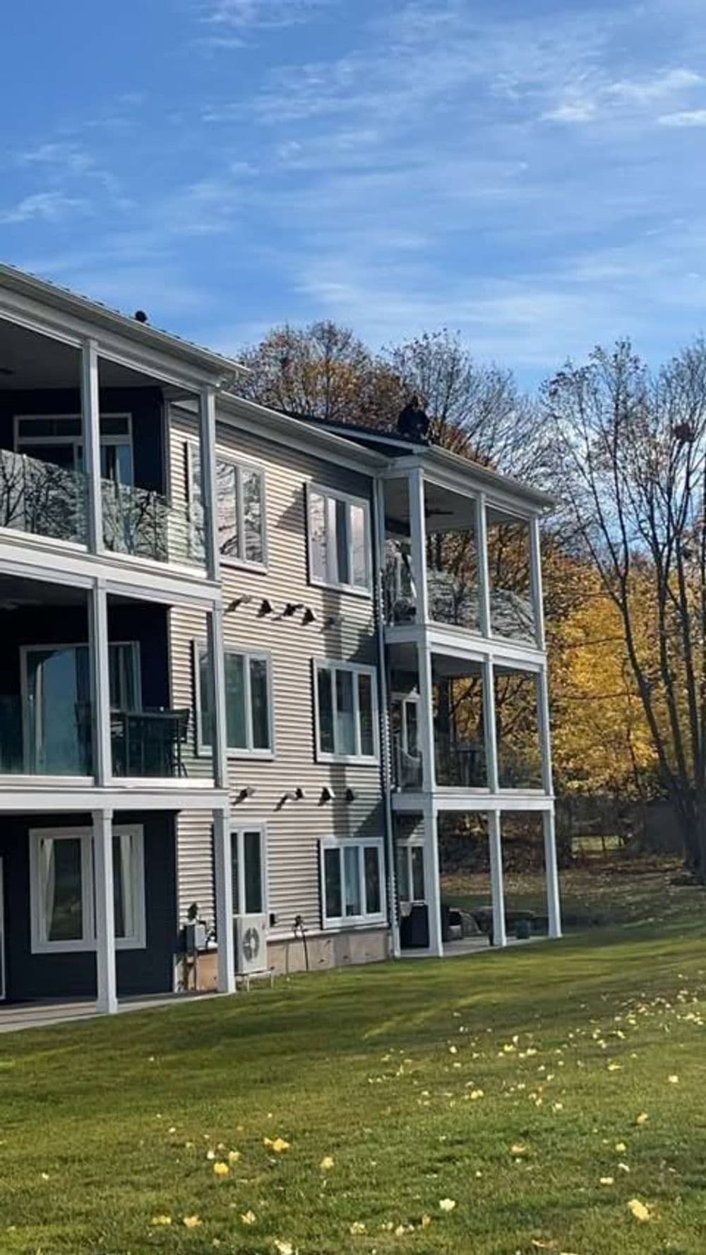 Man on roof of multi-story apartment building with autumn trees in background.