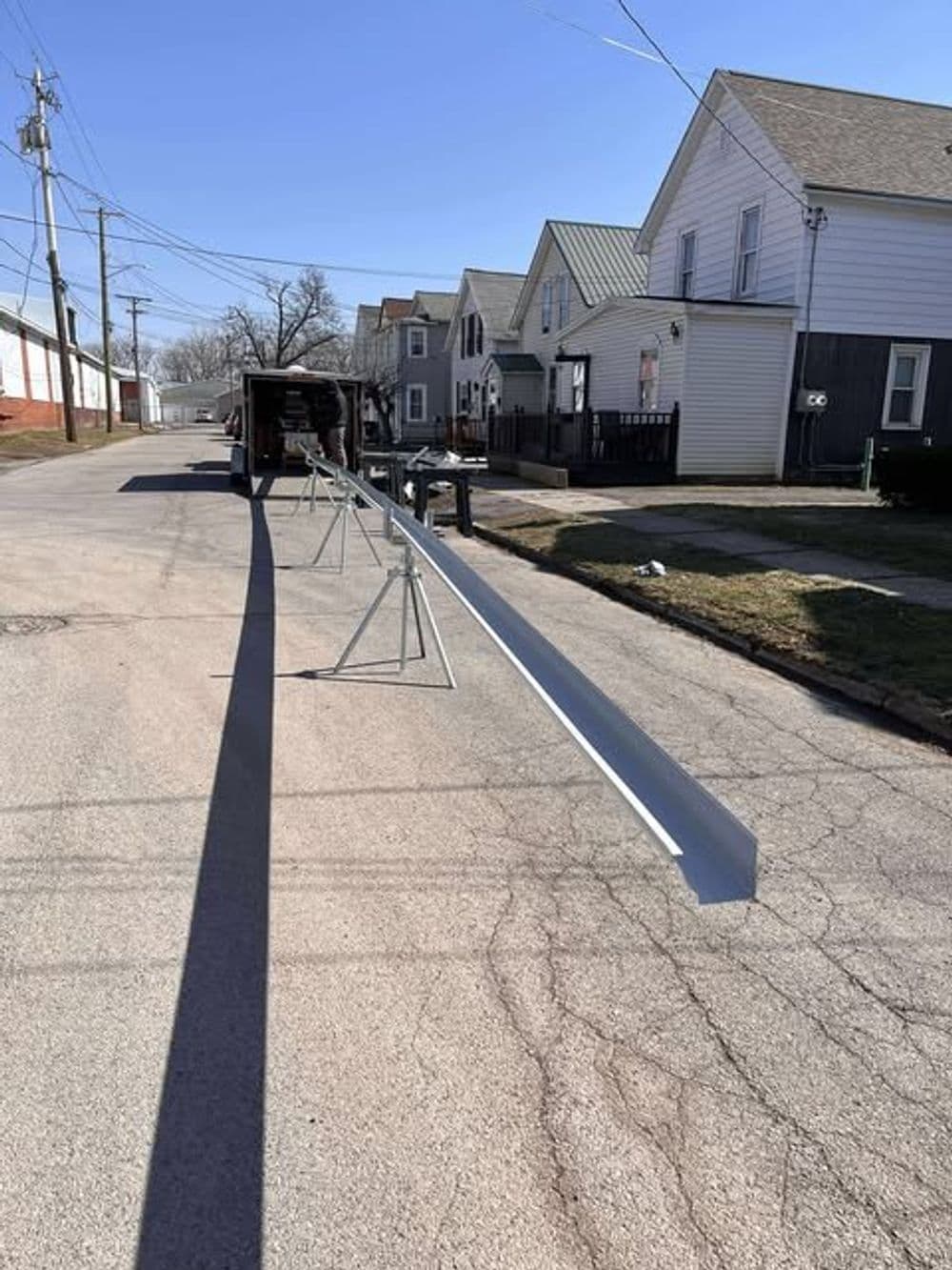 Long metal beam supported by stands on a residential street with houses in the background.