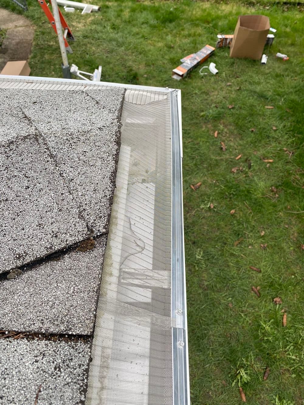 Gutter guard installation on a roof, with tools and materials in a grassy area.