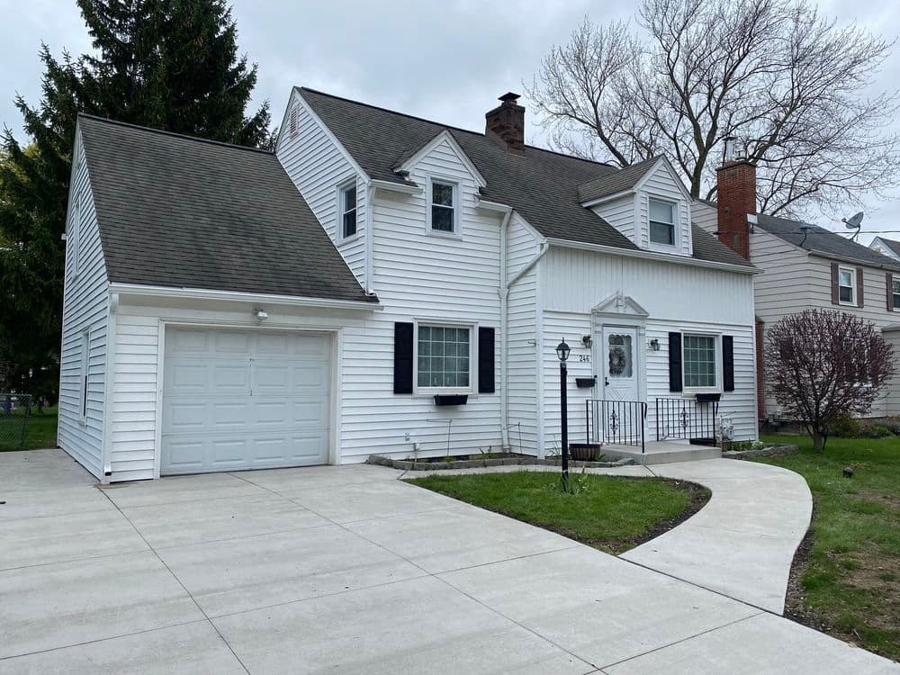 White two-story house with a garage, well-maintained yard, and porch in a suburban neighborhood.